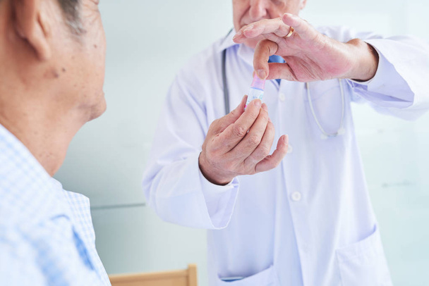 Close-up beeld van de arts tonen kleine fles oogdruppels aan senior patiënt en uit te leggen hoe het te gebruiken - Foto, afbeelding