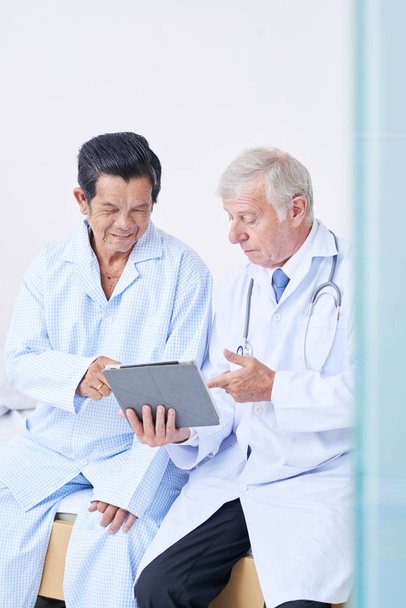 Médico mostrando computador tablet com prescrição na tela para paciente sênior e explicando cada ponto
 - Foto, Imagem