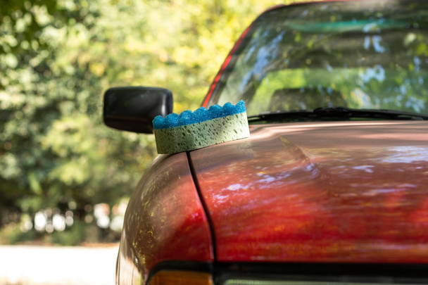 Une éponge de lavage repose sur le capot d'une voiture rouge
. - Photo, image