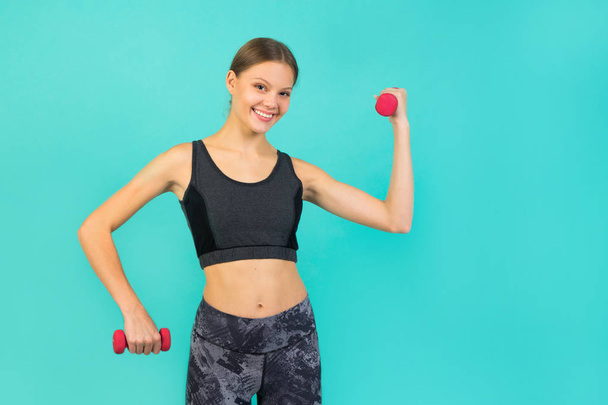 beautiful young slim woman in sportswear on a green background with dumbbells - Foto, imagen