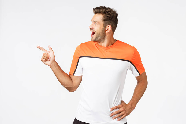 Excited, happy amused masculine sportsman in activewear, attend gym, pointing turning left astonished, gasping from wonder, drop jaw amazed, see amazing promo, product for active lifestyle people - 写真・画像