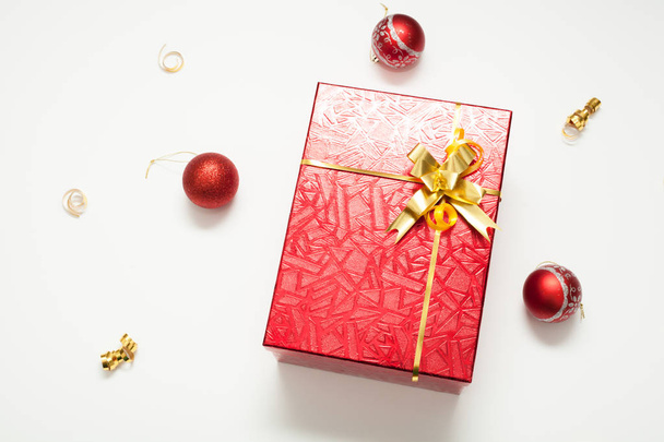Gift box red, shiny with a gold bow, decorated with gold ribbons and Christmas balls, on a white background, there is a place for the inscription. Concept gifts for New year or Christmas. - Φωτογραφία, εικόνα