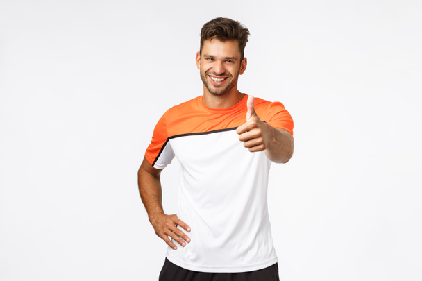 Handsome happy and healthy male athlete, sportsman in good shape showing thumb-up with stretched hand, smiling in approval, fitness trainer encourage client do best during workout in gym - Foto, Imagen