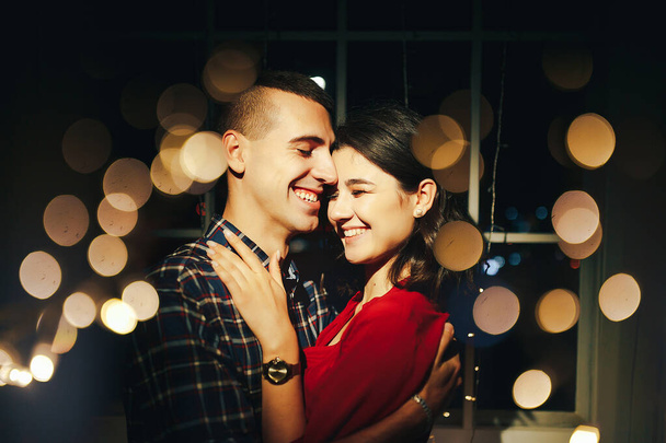 couple in love in the dark between the lights of garlands hugs and kisses. holiday and date for christmas. twelve hours, kiss on new year's eve. in the lights on the background of the window. happines - Foto, imagen