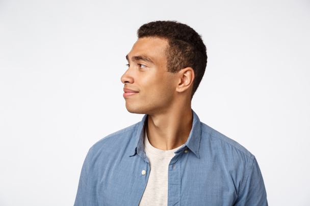 People, fashion and emotions concept. Handsome smiling hispanic guy with short haircut, turn head left, grinning and observe something interesting, contemplate beautiful scenery, white background - Foto, Imagen