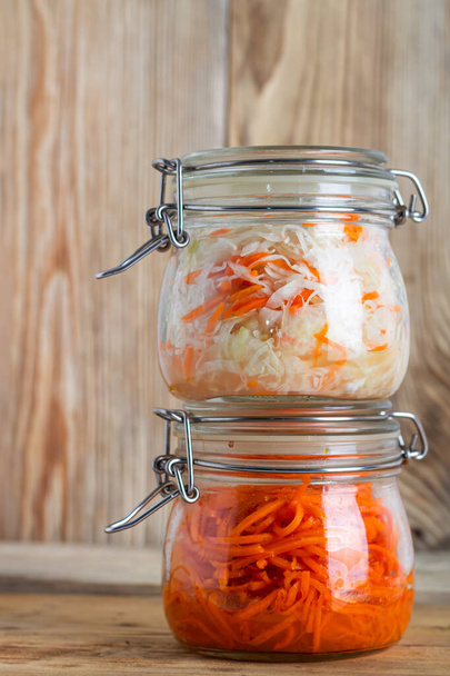 Korean carrots and fermented cabbage in glass jars on a wooden table - Photo, Image