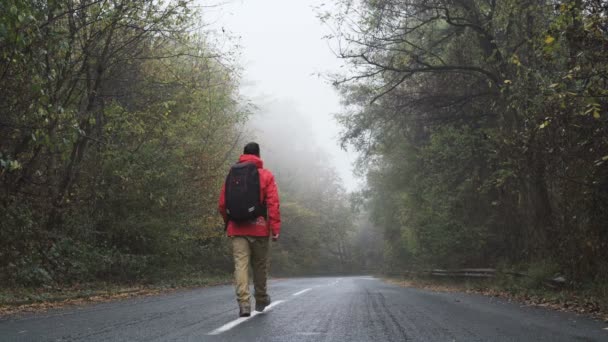 Unbekümmerter Tourist mit roter Jacke läuft gelassen über leere Nebelstraße - Filmmaterial, Video
