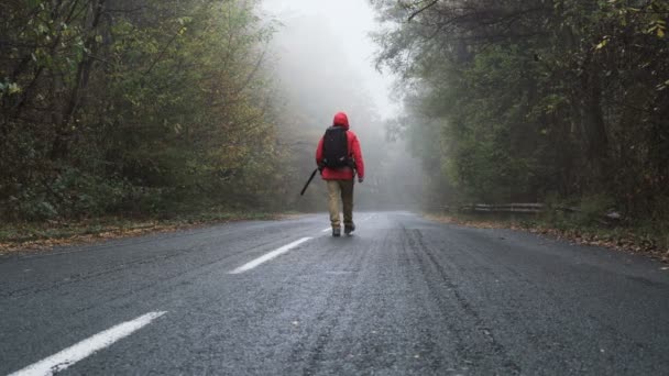Einsamer, verirrter Tourist mit schwarzem Rucksack läuft auf leerer Asphaltstraße - Filmmaterial, Video
