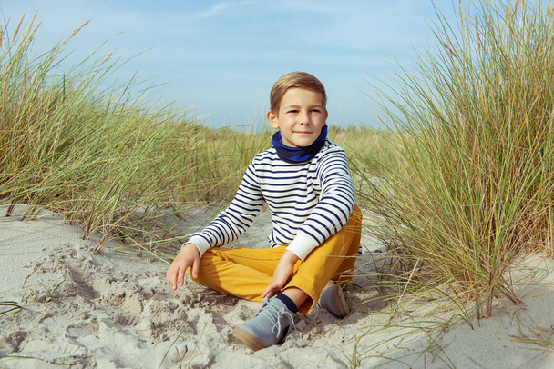Portrait of handsome teenager boy sitting on white sand on beach - Photo, image