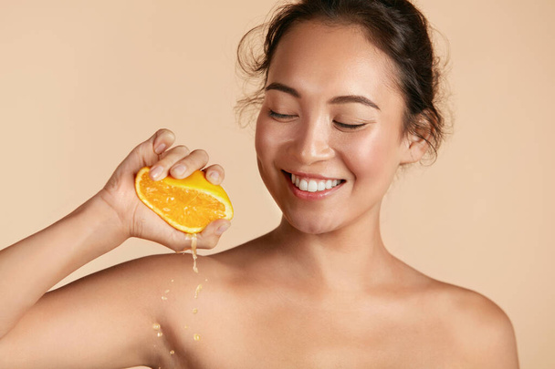Beauty. Woman with radiant face skin squeezing orange portrait - Photo, image