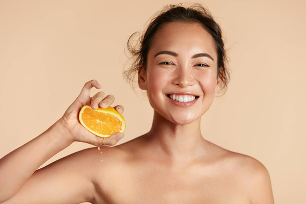 Beauty. Woman with radiant face skin squeezing orange portrait - Foto, Imagen