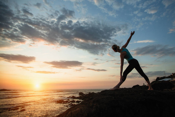 Fitness yoga woman doing exercises on the ocean during amazing sunset. - 写真・画像