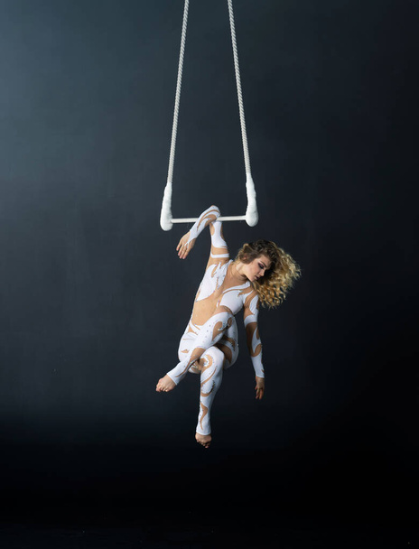 A young girl performs the acrobatic elements in the air trapeze. Studio shooting performances on a black background - Фото, зображення