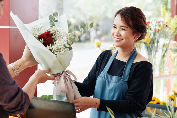 Позитивный работник цветочного магазина дарит заказчику красивый букет с красными розами
 - Фото, изображение