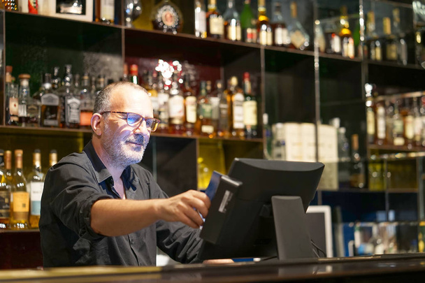 Een restaurant oudere werknemer registreert nieuwe bestelling door cash regis - Foto, afbeelding