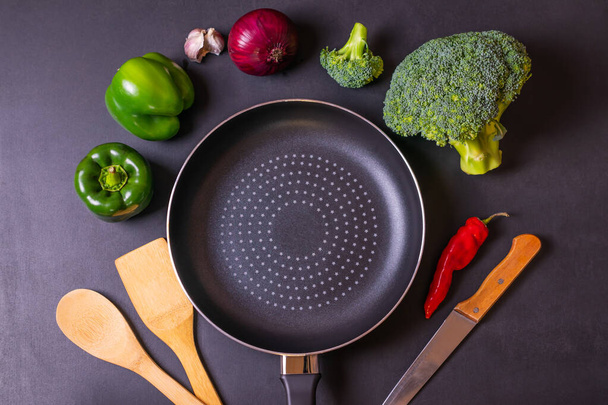 Concepto de cocina fondo negro con sartén, brócoli fresco, pimientos, cebolla roja y ajo
. - Foto, Imagen