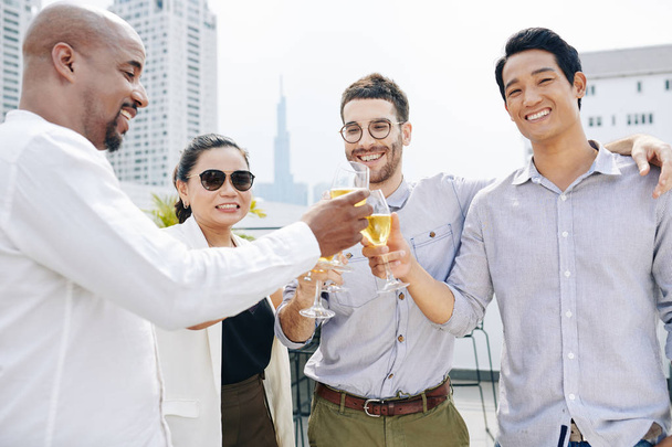 Abraçando colegas multi-étnicos felizes bebendo champanhe e celebrando o grande projeto de acabamento
 - Foto, Imagem