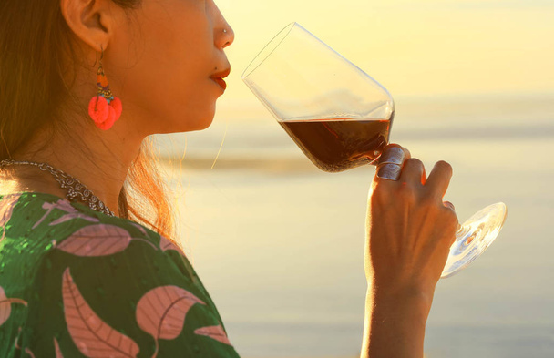 Donna che tiene bicchiere di vino rosso sulla spiaggia durante il tramonto, concetto di celebrazione - Foto, immagini