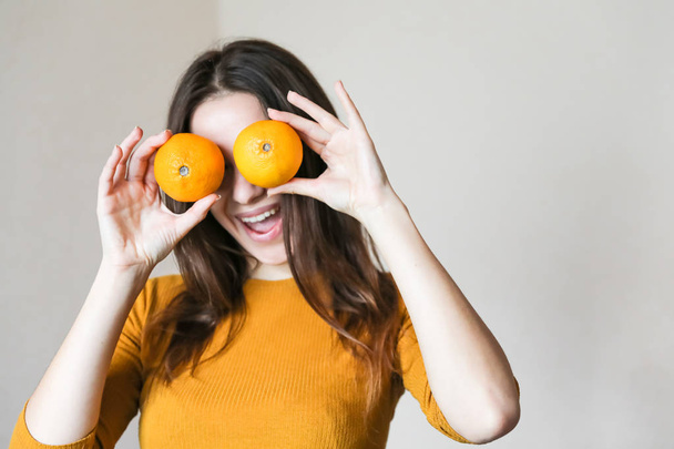 mooi jong meisje gekleed in een oranje T-shirt houdt mandarijnen in haar handen en glimlacht - Foto, afbeelding