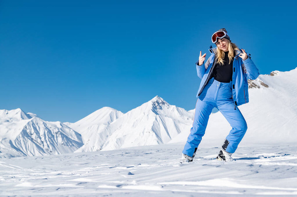 Rubia alegre bailando al aire libre en las montañas. Llevando traje de esquí azul. Delgado cuerpo sexy. Estación de esquí Gudauri
 - Foto, imagen