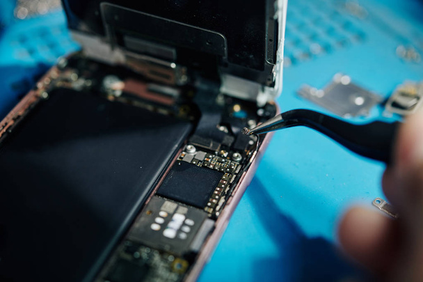 Close-up image of smartphone repairman using tweezers to remove antenna cable when trying to get access to the speaker - Photo, Image