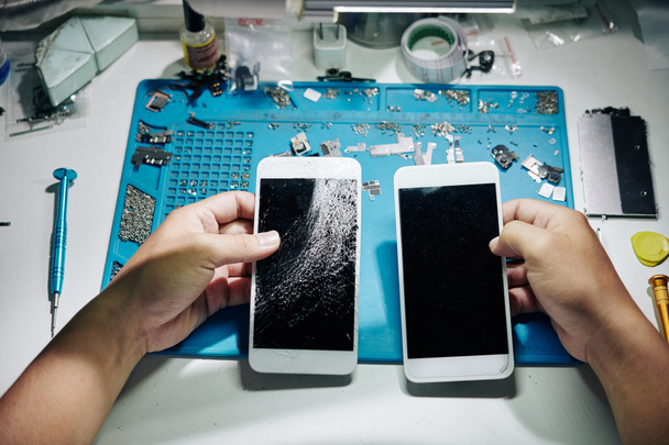Hände von Reparateuren tauschen Smartphone-Bildschirm mit vielen Rissen gegen den neuen - Foto, Bild