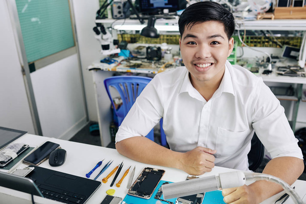 Feliz joven asiático disfrutando de trabajar en el taller de reparación de teléfonos inteligentes
 - Foto, Imagen