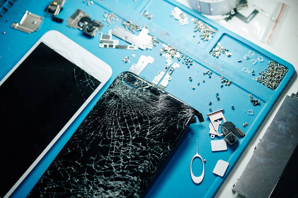 Due smartphone con schermi rotti e piccole viti sul tavolo del riparatore, vista dall'alto
 - Foto, immagini