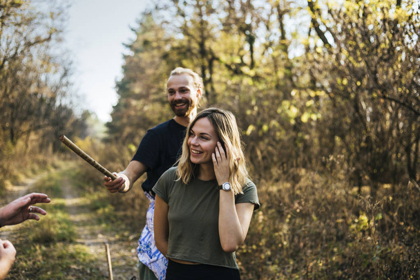 hermosa pareja de adolescentes caminando en el bosque, riendo y dando a alguien caña de madera
 - Foto, imagen