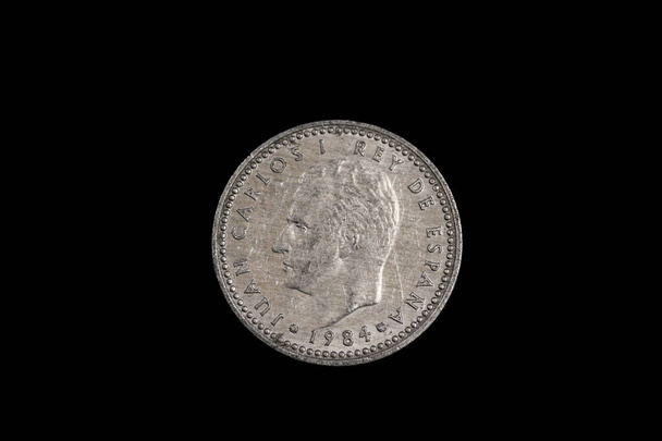 An old Spanish one peseta coin featuring Rey Juan Carlos, shot close up in macro, on a black background - Photo, Image