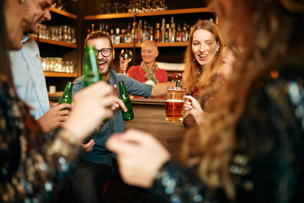 Grupo de amigos bebendo cerveja, conversando e se divertindo no pub. Noite fora
. - Foto, Imagem