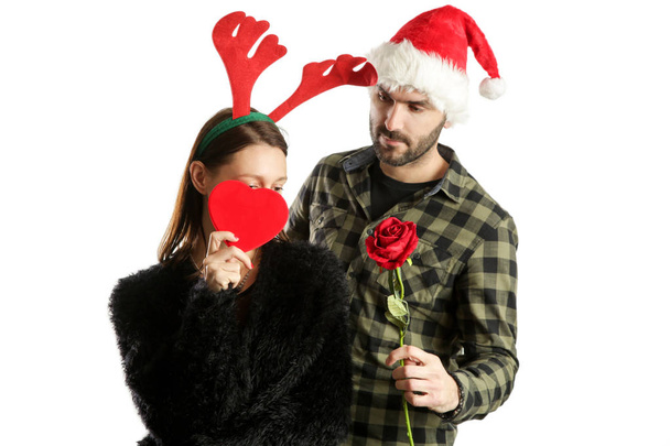 Studio portrait of a young couple wearing santa hat and reindeer headband and exchanging Christmas gifts. Winter holiday gifting concept. - Foto, Imagem