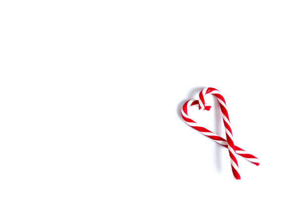 Δύο χριστουγεννιάτικες κόκκινες και άσπρες καραμέλες, χριστουγεννιάτικες καραμέλες διπλωμένες σε σχήμα καρδιάς σε λευκό φόντο. τόπος για κείμενο - Φωτογραφία, εικόνα