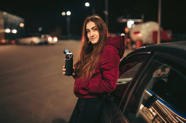 Portrait of woman driver with thermos bottle at gas station, night time - Zdjęcie, obraz