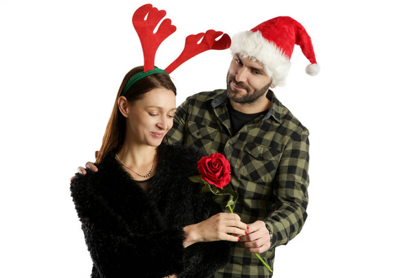 Studio portrait of a young couple wearing santa hat and reindeer headband and exchanging Christmas gifts. Winter holiday gifting concept. - Photo, Image