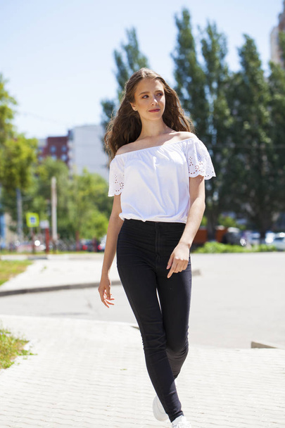 Young beautiful brunette woman in jeans and white blouse walking - Fotó, kép