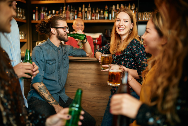 Grupa przyjaciół pije piwo, rozmawia i dobrze się bawi w pubie. Noc poza domem. - Zdjęcie, obraz