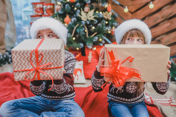 Close up photo of son and daughter who prepared Xmas gifts for their parents and are showing them to the camera, looking proud of what theyve done. - Фото, изображение