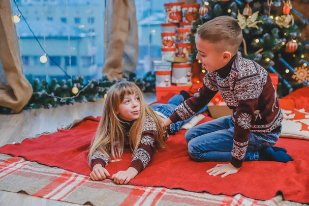 Cute photo of brother and sister enjoying time together at fir-tree on Christmas evening. - Fotoğraf, Görsel