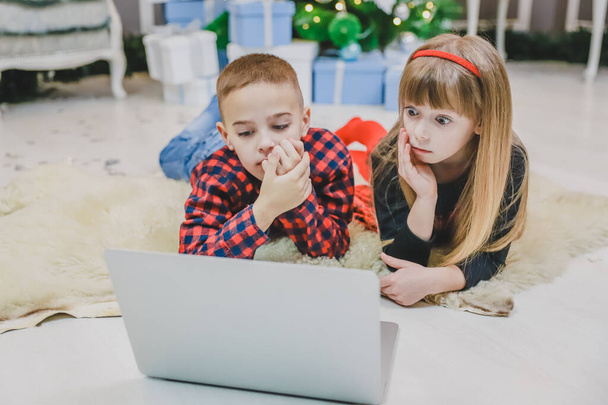 Warm photo of pretty siblings watching new year movie while laying on the carpet under Christmas fir. - Foto, imagen
