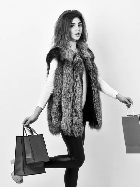 Fashionista buy fashionable clothes in shop. Girl makeup face long hairstyle wear fur vest white background. Woman shopping luxury boutique. Lady hold shopping bags in hands. Shopping concept - Foto, Bild