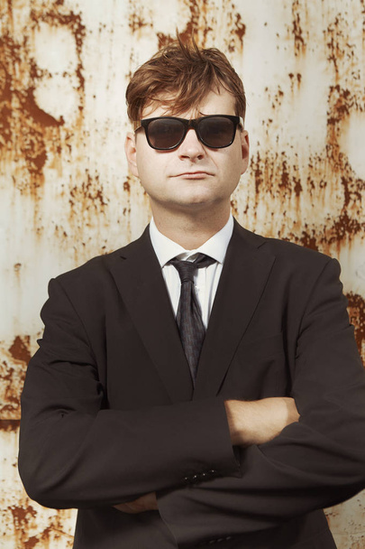 Man in suit and glasses posing by the rusty wall - Фото, изображение