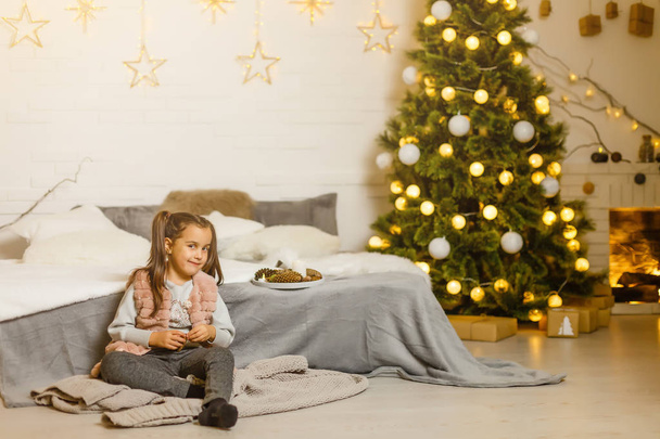 little girl sits in a room decorated for christmas - Foto, Imagen