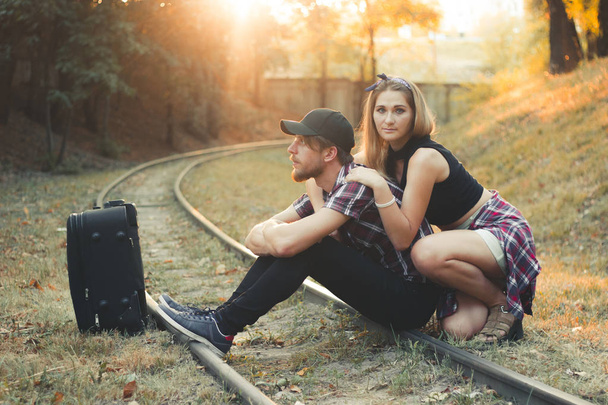 Young couple with suitcase late on train. Lovers are waiting for the train on rails. Desperate travelers lagged behind the train in the fall at sunset. - Photo, Image