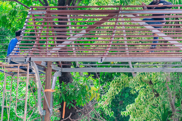 Сварщик и художник помогают построить крышу под большим деревом манго. - Фото, изображение