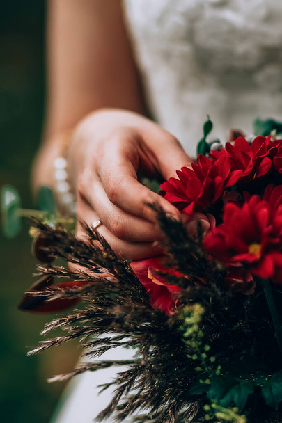 Bride holding bouquet with vinous flowers in composition with green and brown herbs - 写真・画像