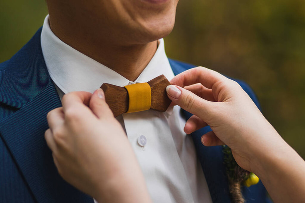 Заботливая невеста выпрямляет деревянный галстук-бабочку жениху
 - Фото, изображение
