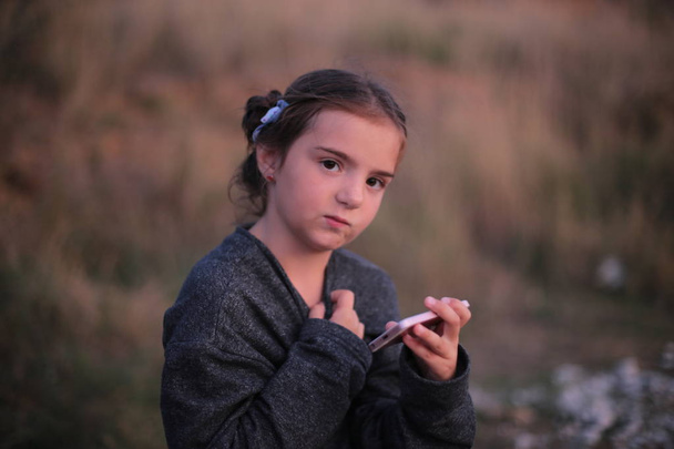 una chica de siete años con diferentes emociones en su cara juega en el teléfono
 - Foto, Imagen