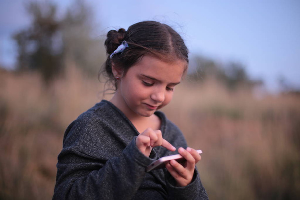 Ένα κορίτσι επτά ετών με διαφορετικά συναισθήματα στο πρόσωπό της παίζει στο τηλέφωνο - Φωτογραφία, εικόνα