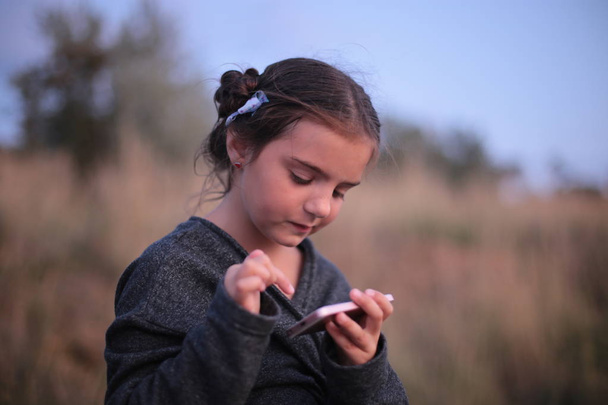 a girl of seven years with different emotions on her face plays on the phone - Photo, Image